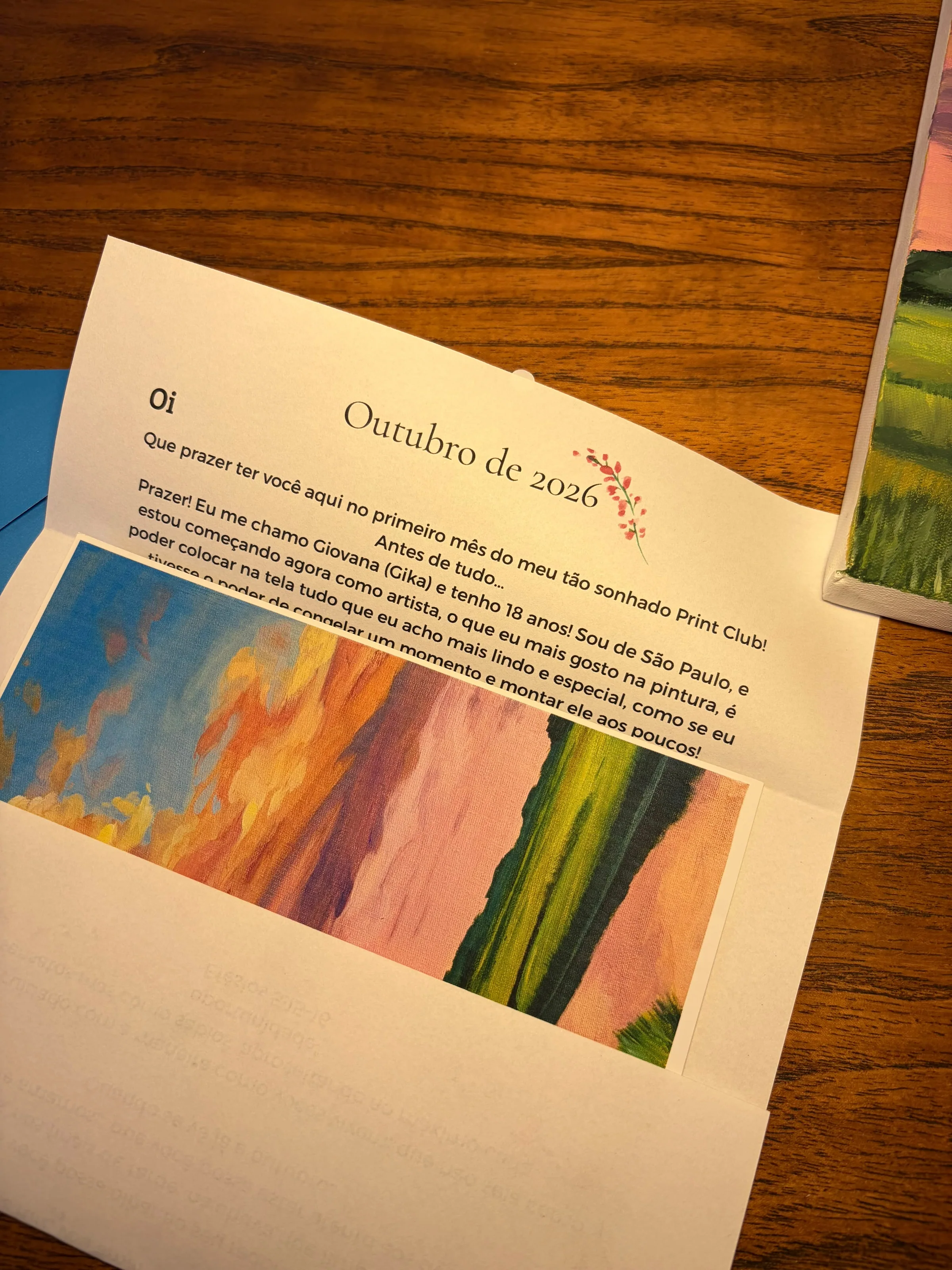Carta de Outubro de 2026 aberta sobre a mesa, com um mini print da pintura dentro do envelope azul.